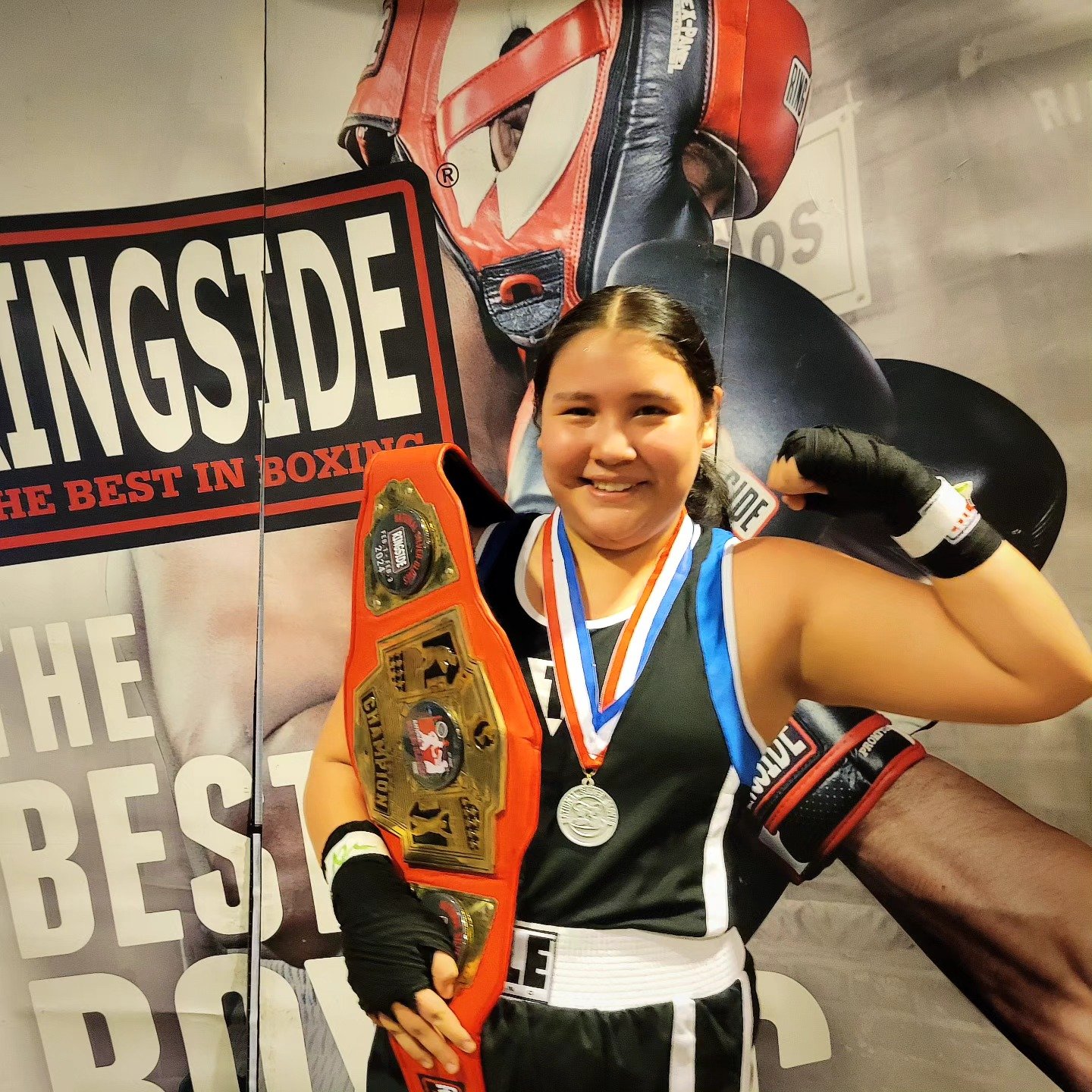 photo of young girl holding boxing belt flexing infront of promotional boxing poster