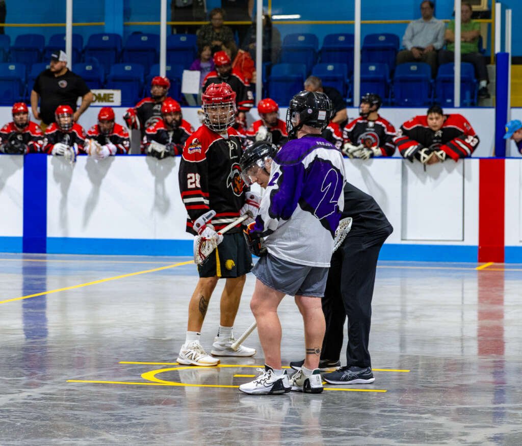 Lacrosse players and a referee getting ready for a face off.