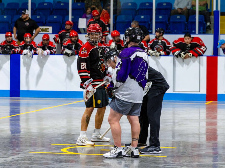 Lacrosse players and a referee getting ready for a face off.